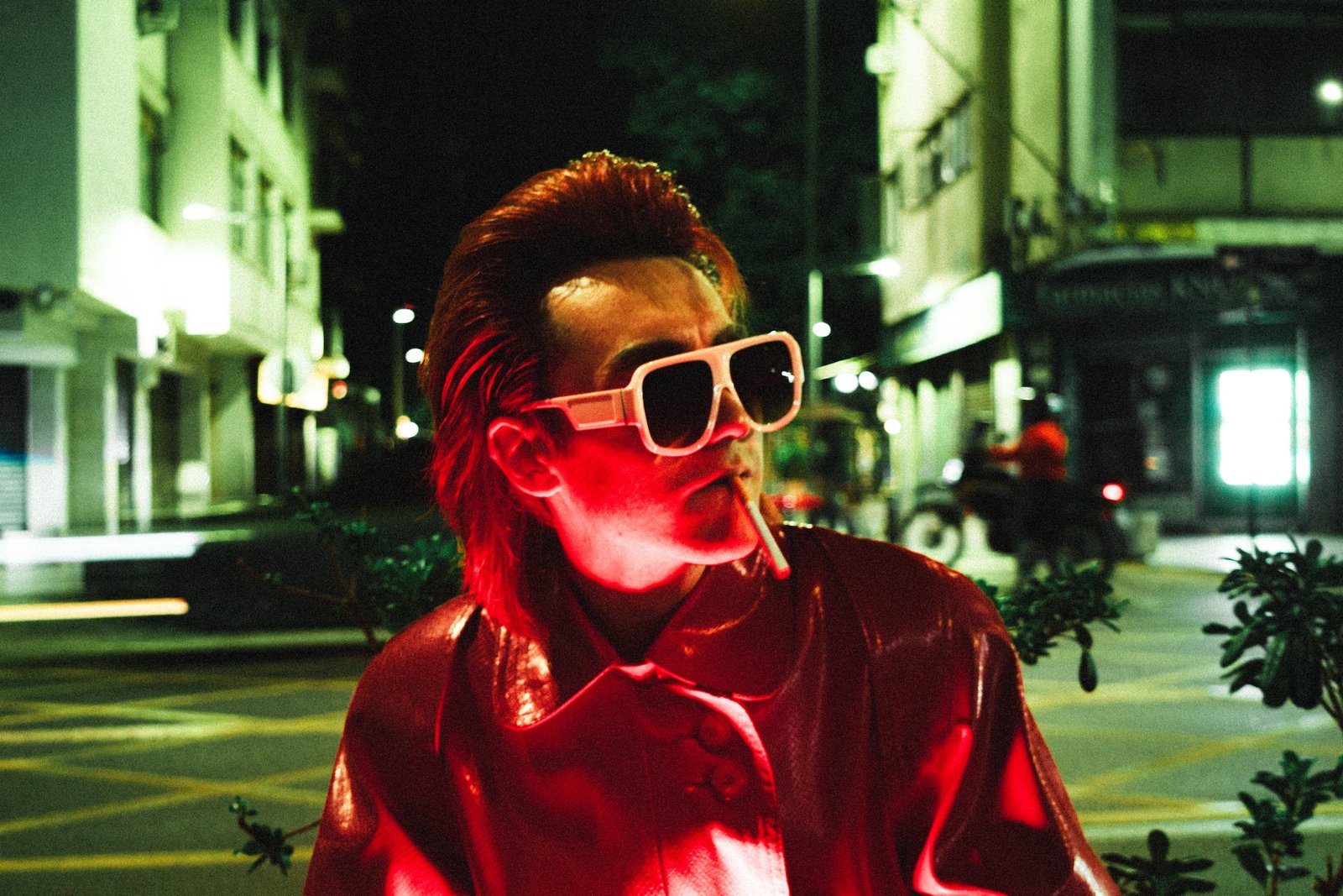Gaspar Luna caracterizado como el diablo: chaqueta roja de charol, gafas y un cigarrillo, bajo neón rojo y verde